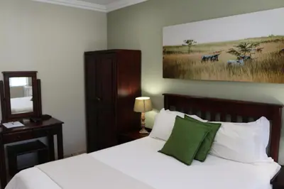 a bedroom with a bed with white sheets and green pillows at Hummingbird's Nest in Nelspruit