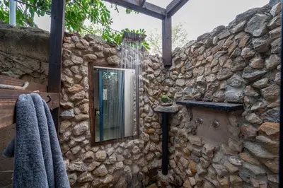 a bathroom with a mirror on a stone wall at Foxy Crocodile Bush Lodge & Kruger Safaris in Marloth Park