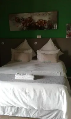 a bed with white sheets and pillows on it at Tassili Lodge in Kempton Park