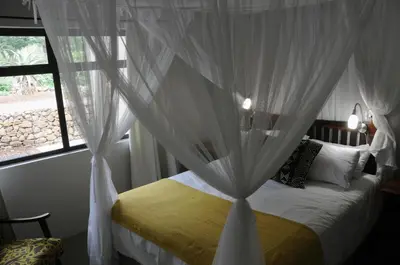 a bedroom with a bed with white curtains and a window at Ukuthula Hideaway in Kampersrus AH