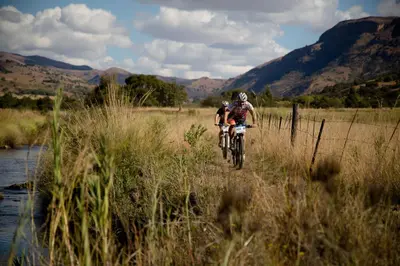 two people riding bikes in a field next to a river at Verlorenkloof in Dullstroom