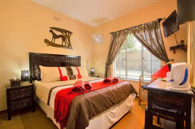 a bedroom with a bed with red sheets and a window at All over Africa Guest house in Kempton Park