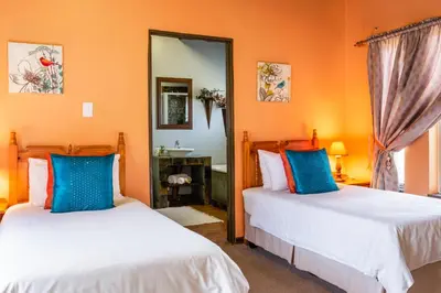 two beds in a room with orange walls and blue pillows at Aberfeldy Bed & Breakfast in Midrand