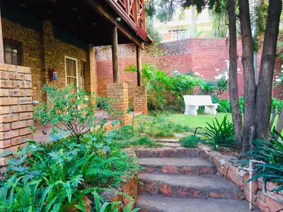 a garden with a brick house with a white bench at Amper Bo Guest House in Pretoria