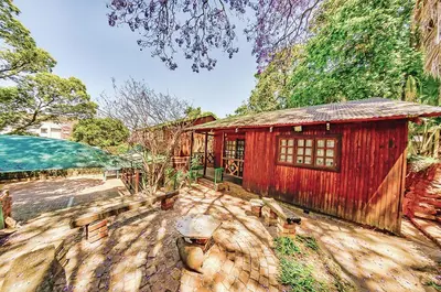 a house with a red building on a patio at Amper Bo Guest House in Pretoria