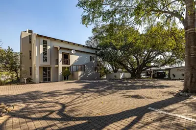a white building with a tree in front of it at Francolin Lodge in Nelspruit