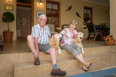 a man and a woman sitting on steps with two dogs at Porcupine Ridge Guest House in Sabie
