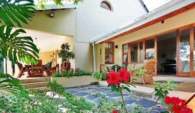 a house with a patio with red flowers in the yard at Porcupine Ridge Guest House in Sabie
