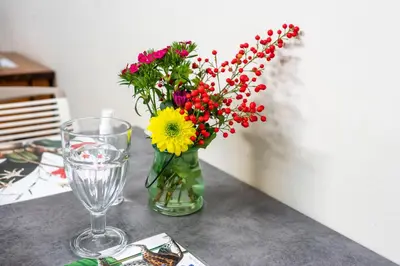 a vase filled with flowers on a table with a glass at Polo Guest House in Polokwane