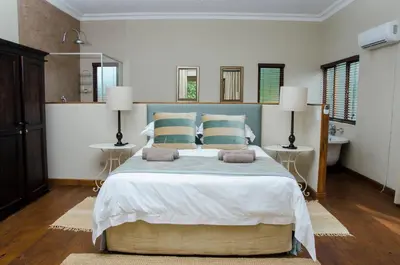 a bedroom with a large bed with two lamps and a sink at Villa Rostrata-on-Lake in Hazyview