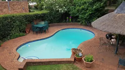 a swimming pool on a brick patio with a table at Homestead Lake Cottage in Benoni