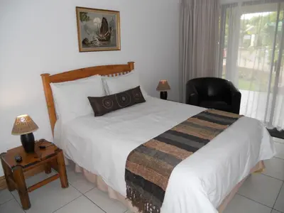 a bedroom with a bed and a chair and a window at Homestead Lake Cottage in Benoni