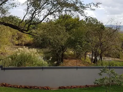 a fence with a view of a pond and trees at Holiday Flat Stormvoel 547 in Hazyview