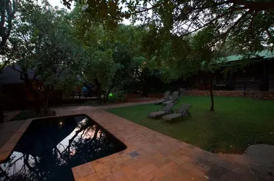 a patio with two benches and a pond in a yard at Tuskers Bush Lodge B&B in Hartbeespoort