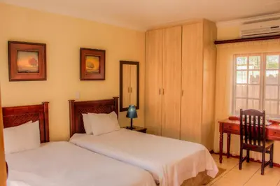 a bedroom with two beds and a desk and a window at Marlot Guest House in Polokwane