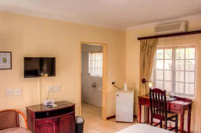 a living room with a television and a kitchen with a refrigerator at Marlot Guest House in Polokwane