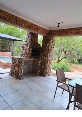 a stone fireplace on a patio with a table and chairs at Lion King in Marloth Park