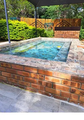 a brick wall around a swimming pool with an umbrella at Lion King in Marloth Park