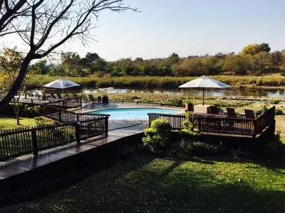 a swimming pool with tables and umbrellas next to a river at Sabie River Bush Lodge in Hazyview