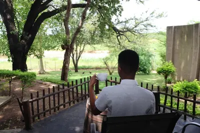 a man sitting on a bench drinking a cup of coffee at Sabie River Bush Lodge in Hazyview