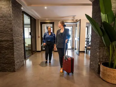 two women walking down a hallway with a suitcase at ANEW Hotel Witbank Emalahleni in Witbank