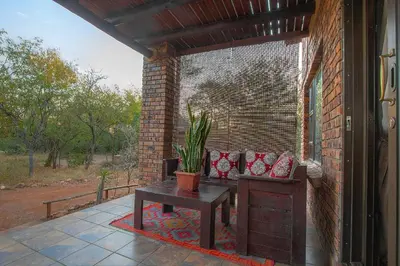a patio with a table and a bench on a brick wall at Wildgoose Lodge in Marloth Park