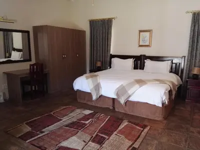 a bedroom with a large bed and a desk at Nooitgedacht Trout Lodge in Lydenburg