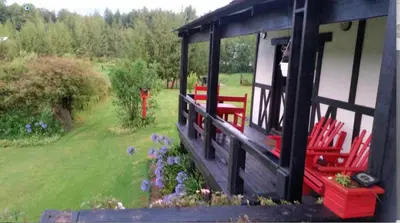 a house with a porch with red chairs in a yard at Woodcutters Guest House in Haenertsburg