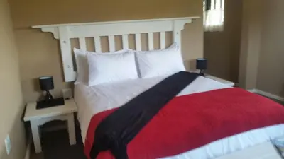 a bedroom with a large bed with a red and white blanket at Woodcutters Guest House in Haenertsburg