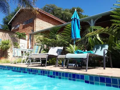 a pool with chairs and an umbrella next to a house at Vivian's Cottage in Pretoria