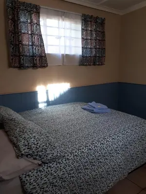a bed in a bedroom with a window and a blanket at Vivian's Cottage in Pretoria