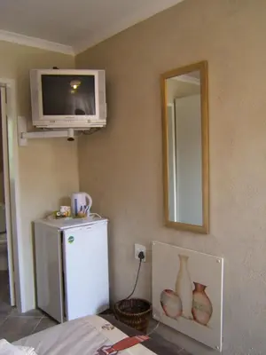a room with a tv and a refrigerator and a mirror at Vivian's Cottage in Pretoria
