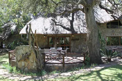 a stone house with a table and chairs under a tree at Moholoholo Ya Mati in Kampersrus AH