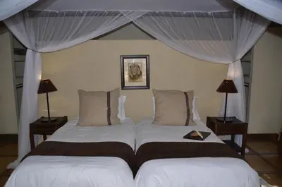 a bedroom with two beds with curtains and lamps at Moholoholo Forest Camp in Hoedspruit