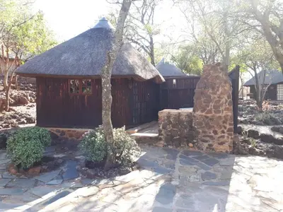 a small building with a thatch roof and a stone wall at ThabaNkwe Bushveld Inn in Thabazimbi
