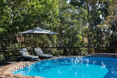 a swimming pool with two chairs and an umbrella at Ndlovu Safari Lodge in Welgevonden Game Reserve