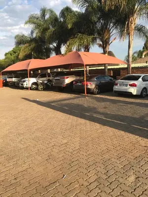a row of cars parked in a parking lot with red umbrellas at Platinum Lodge Polokwane in Polokwane
