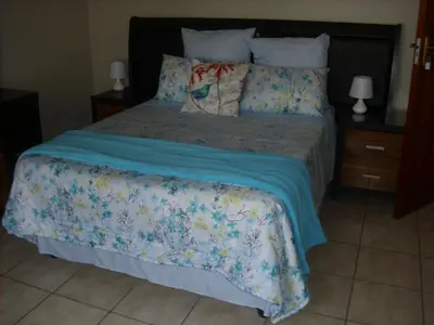 a bedroom with a bed with a blue blanket and pillows at Tropical Paradise Guest House in Nelspruit
