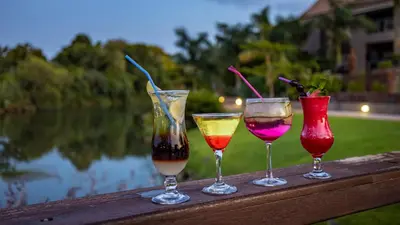 three wine glasses sitting on a wooden rail next to a lake at Nkomazi Kruger Lodge & Spa in Malelane