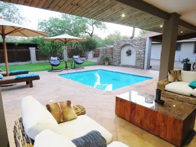 a patio with a pool and chairs and an umbrella at Wild Dog Guest Lodge in Hoedspruit