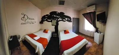 two beds in a room with a tree on the wall at Casa Feliz in Mokopane