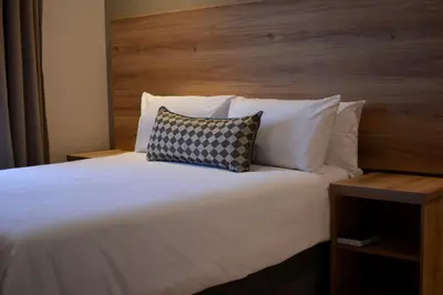 a bedroom with a white bed with a wooden headboard at Regal Inn Hotel Midrand in Midrand