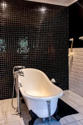 a white bath tub in a black tiled bathroom at The Porcupine Porch in Marloth Park