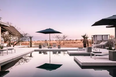 a pool with tables and umbrellas and chairs at Kruger Sunset Lodge in Hectorspruit