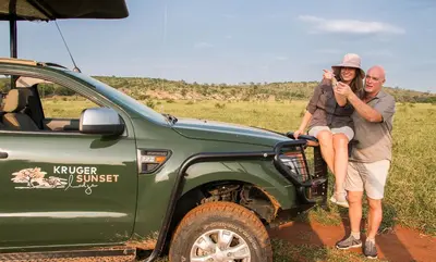 a man and woman sitting on the back of a green truck at Kruger Sunset Lodge in Hectorspruit