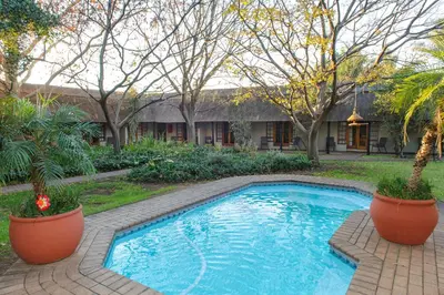 a swimming pool in a yard with trees and a house at Safari Club Guest Lodge OR Tambo International Airport in Kempton Park