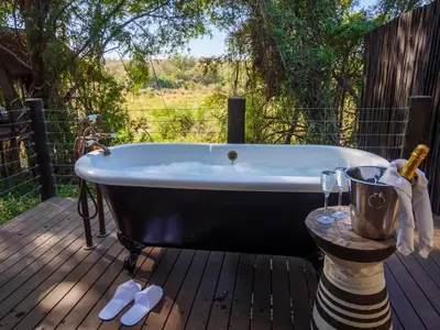 a bath tub sitting on a deck with wine glasses at Jock Safari Lodge in Skukuza