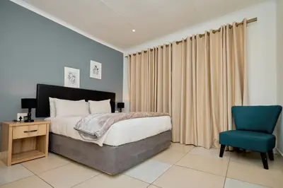a bedroom with a bed and a blue chair at Menlyn Maine: The Exquisite Lunette in Pretoria
