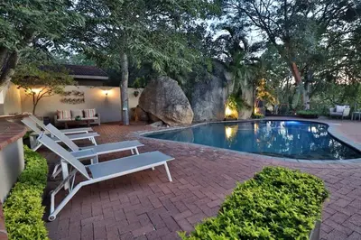a swimming pool with two lounge chairs and a rock at La Roca Guest House in Nelspruit
