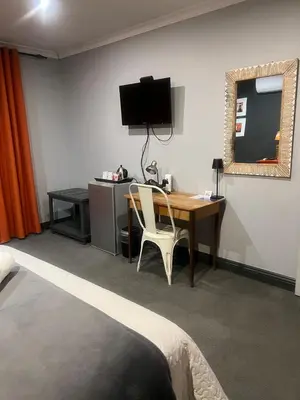 a bedroom with a desk and a television on a wall at Koru Guesthouse in Pretoria